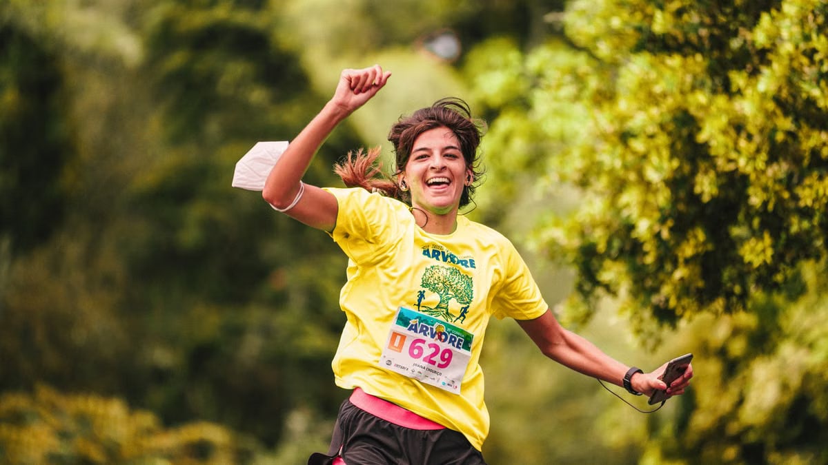 Joyful female runner in yellow participates in an outdoor race amidst lush greenery, embodying athletic enthusiasm.